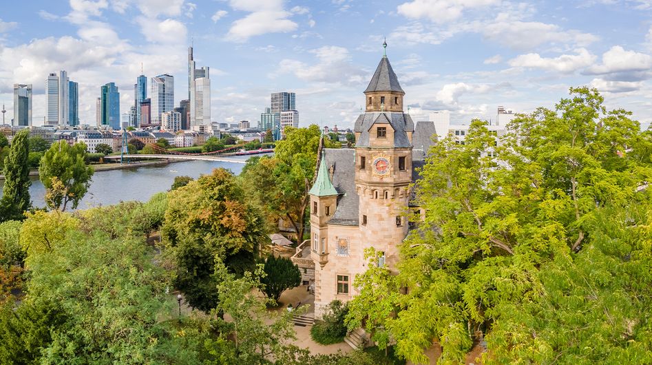 Historic building surrounded by green trees, in the background the Main River and the financial district of Frankfurt am Main