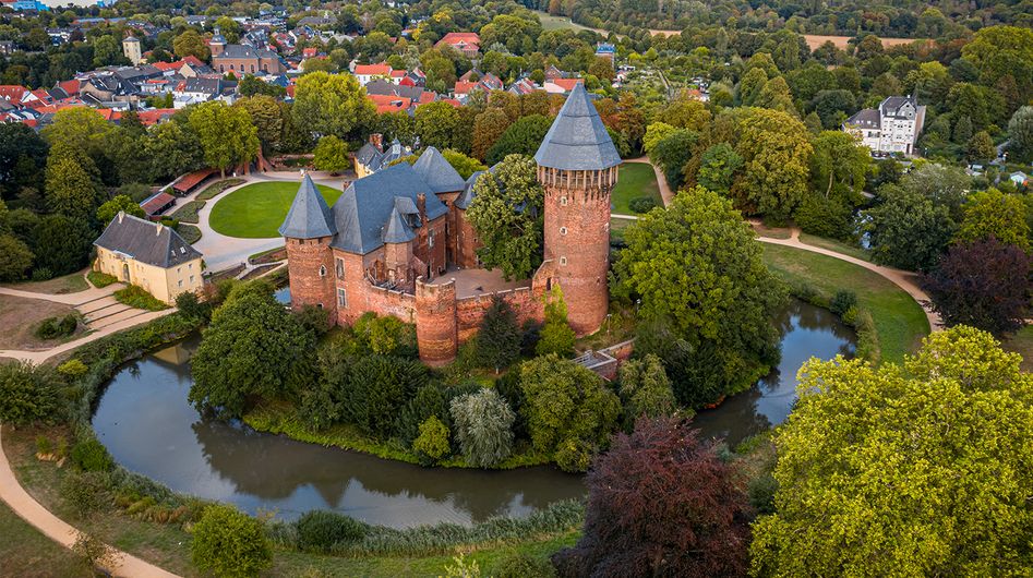 Linn Castle with moat, surrounded by greenery and the buildings of Krefeld in the background