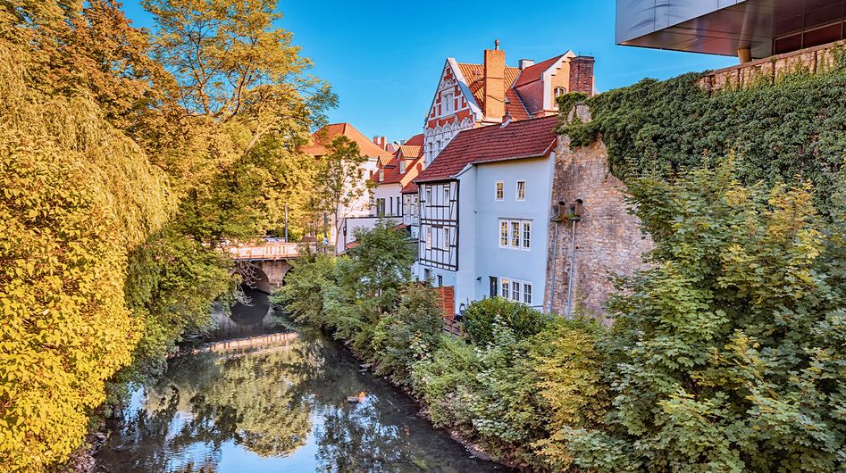 Ein ruhiger Flusslauf in Osnabrück umgeben von Bäumen, am Ufer historische Gebäude