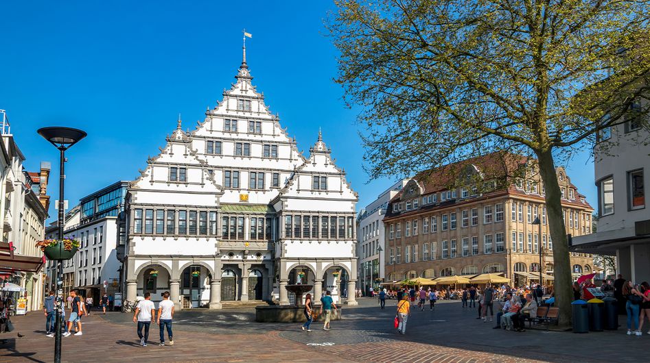 People stroll across a square in Paderborn surrounded by historic buildings.