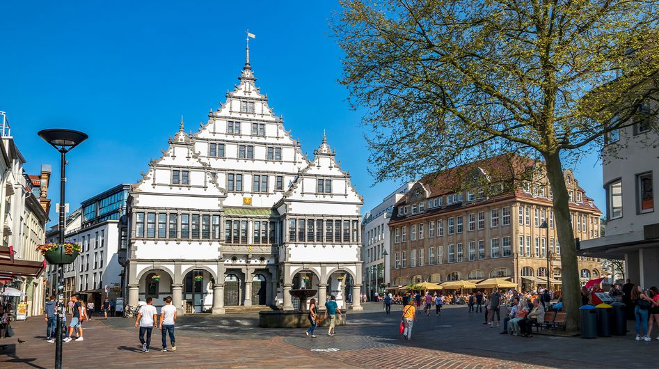 Menschen schlendern über einen Paderborner Platz umgeben von historischen Gebäuden.