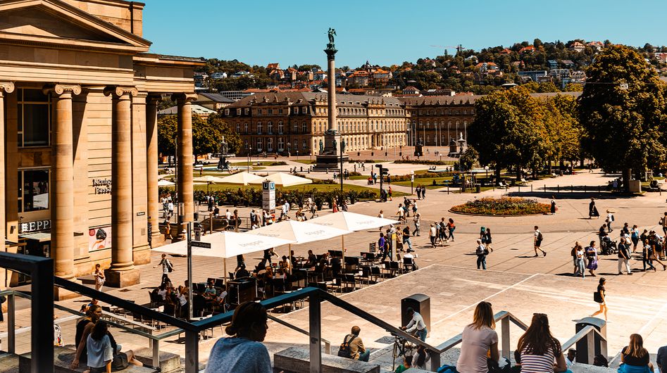 Der belebte Stuttgarter Schlossplatz unter blauem Himmel, in der Mitte die Jubiläumssäule