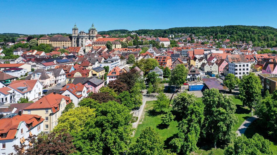 Blick von oben auf einen grünen Park mit Straßenzügen und historischen Gebäuden im Hintergrund