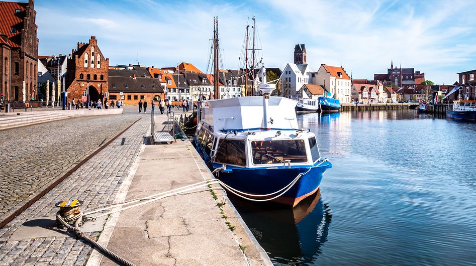 Am Ufer verankerte Schiffe mit historischen Gebäuden in Wismar im Hintergrund